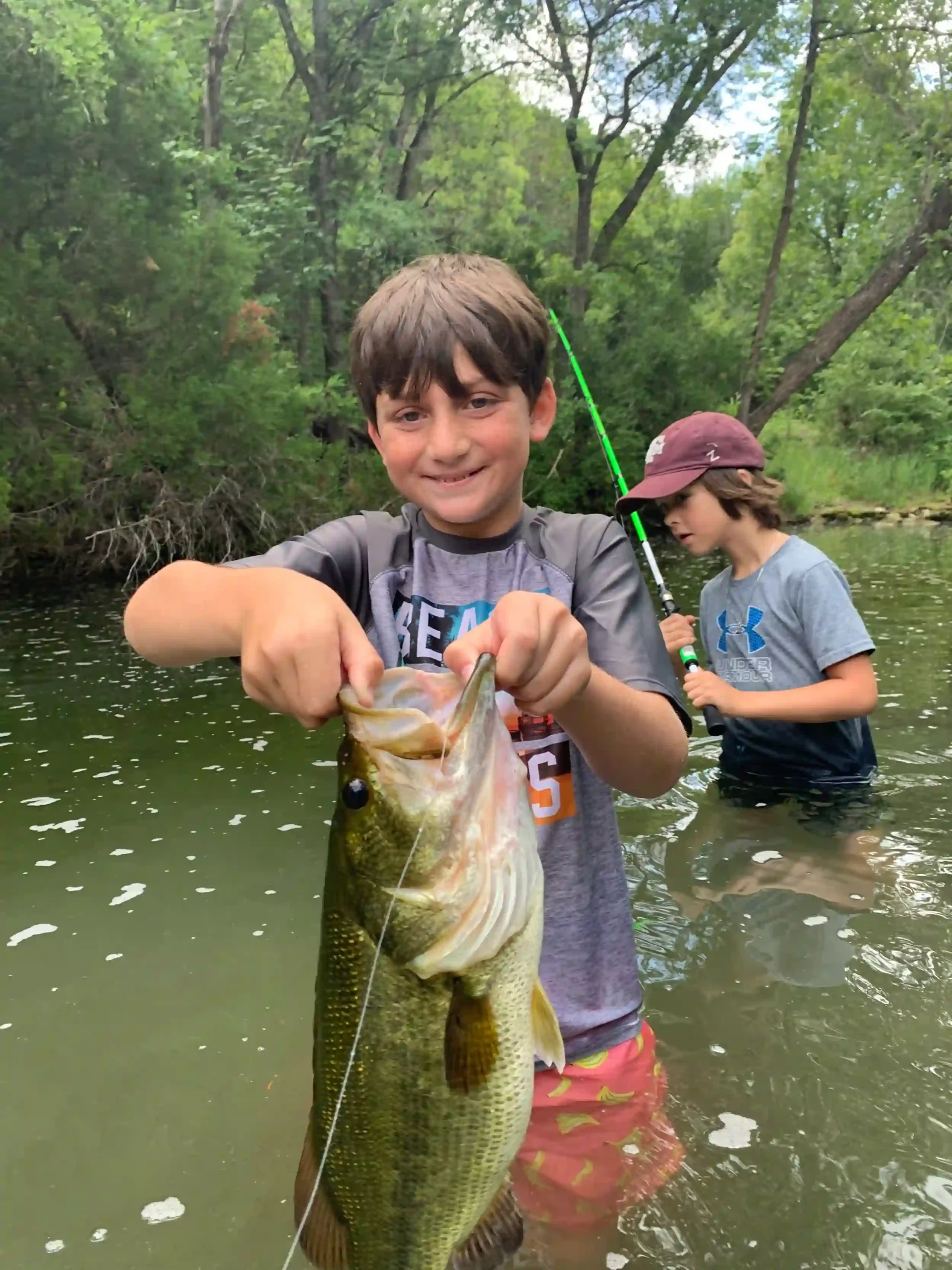 A young boy holding a fish, participating in Hill Country Fishing Camps' summer camp.